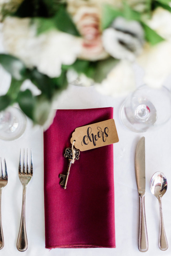 photo of a table with a red wine napkin and cutlery, with a key bottle opener on top. Wedding ideas on a budget