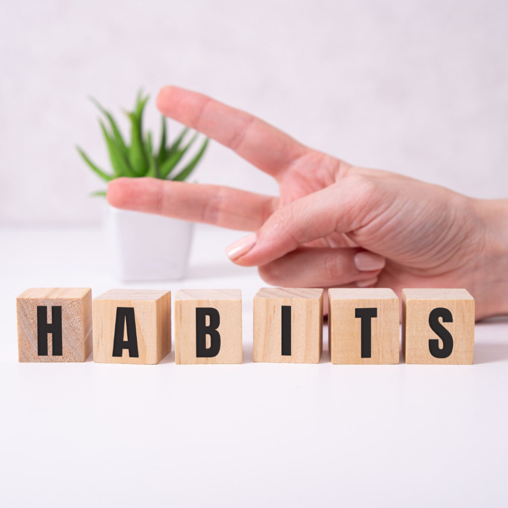 healthy habits - the word habit spelt out on wooden blocks, hand doing peace sign, with a green plant in the background.