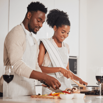 couple wearing white aprons while cooking. With two glasses of red wine. date night ideas for married couples