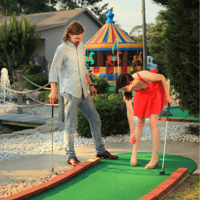 guy in light blue shirt and women in red dress playing mini golfing outdoors. married couple date night ideas