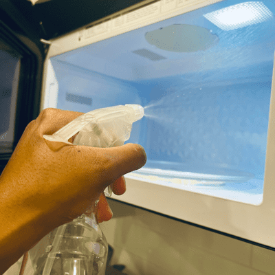 clean with vinegar - spraying bottle filled with water and vinegar cleaning the microwave 