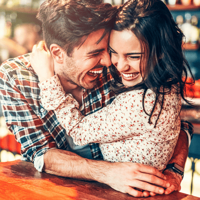 Couple at a bar, laughing and holding each other. 
