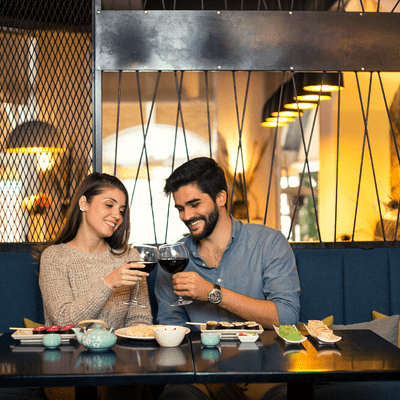 couple at a restaurant eating sushi, cheering with a glass of red wine 