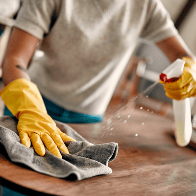 girl spraying a cleaning solution on a wooden table then wiping it with a grey microfiber cloth. Apartment spring cleaning checklist 
