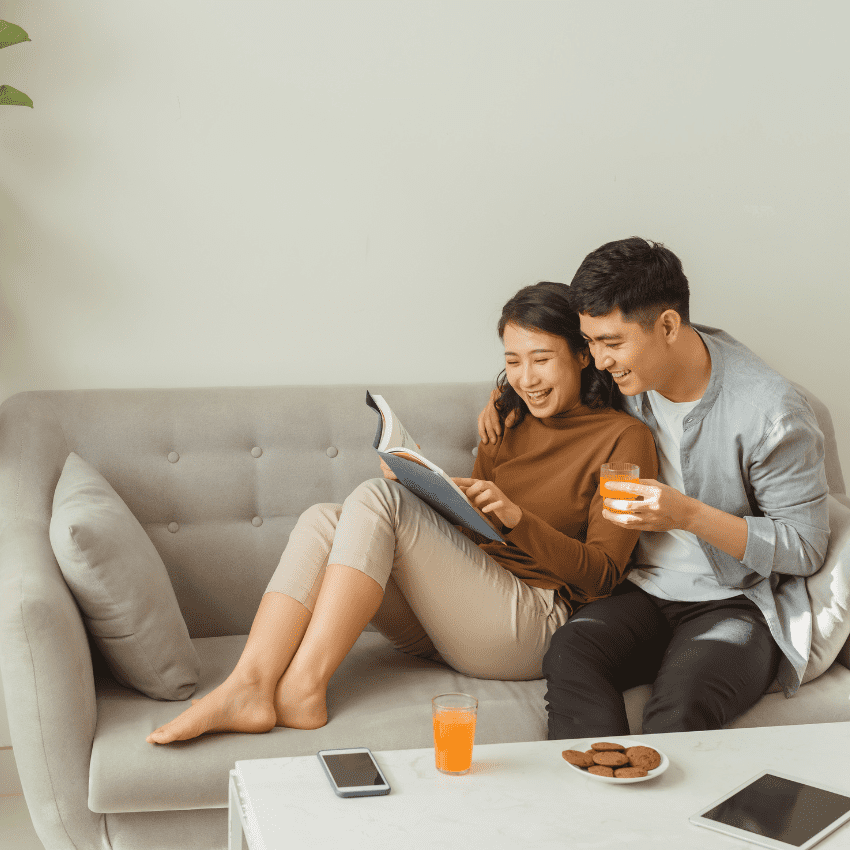 photo of a guy and girl lounging on the couch looking at a book. Wedding registry checklist