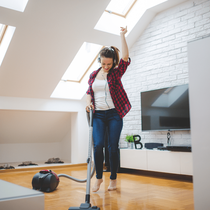 girl dancing around with headphones in her ears while vacuuming the hardwood floors. apartment moving cleaning hacks.