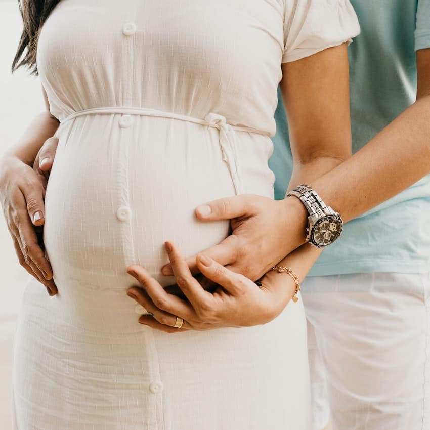 Man holding his pregnant wife's belly. Family planning questions.