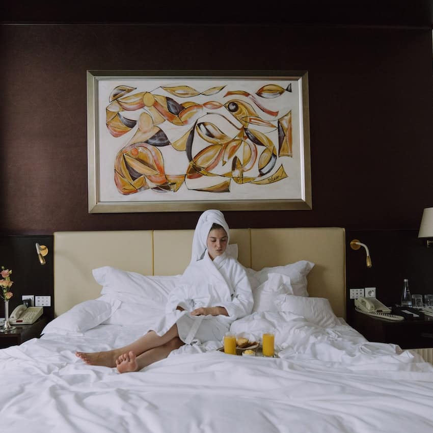 women sitting on her bed with a tray of breakfast items, in a white robe and white towel over her head. wedding registry for house.