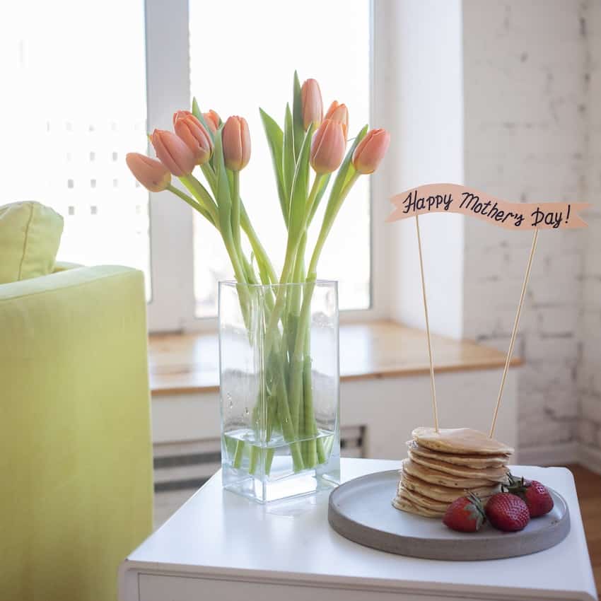 Photo of a stack of pancake, with a sign that says "Happy mothers day" with pink tulips. mother's day celebration ideas.