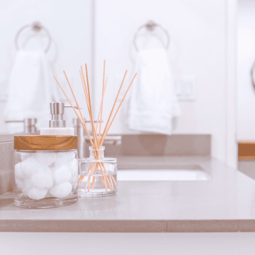 photo of a bathroom sink with glass jar containers with cotton balls, soap dispenser and diffuser. Organize under the bathroom sink. 