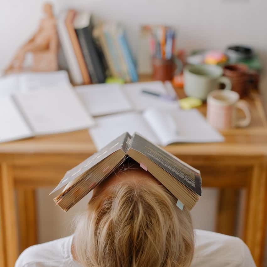 Girl resting a textbook on top of her head. Freshman tips for college.