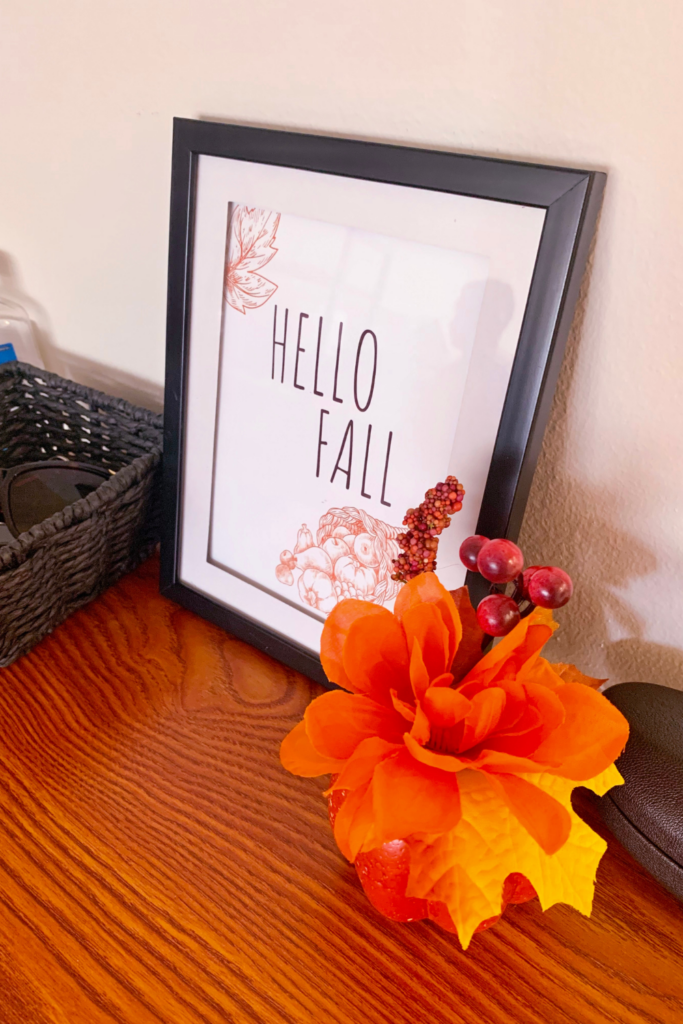 photo of a frame with the saying "Hello Fall" inside with a artificial pumpkin beside it. Apartment decor ideas for fall. 