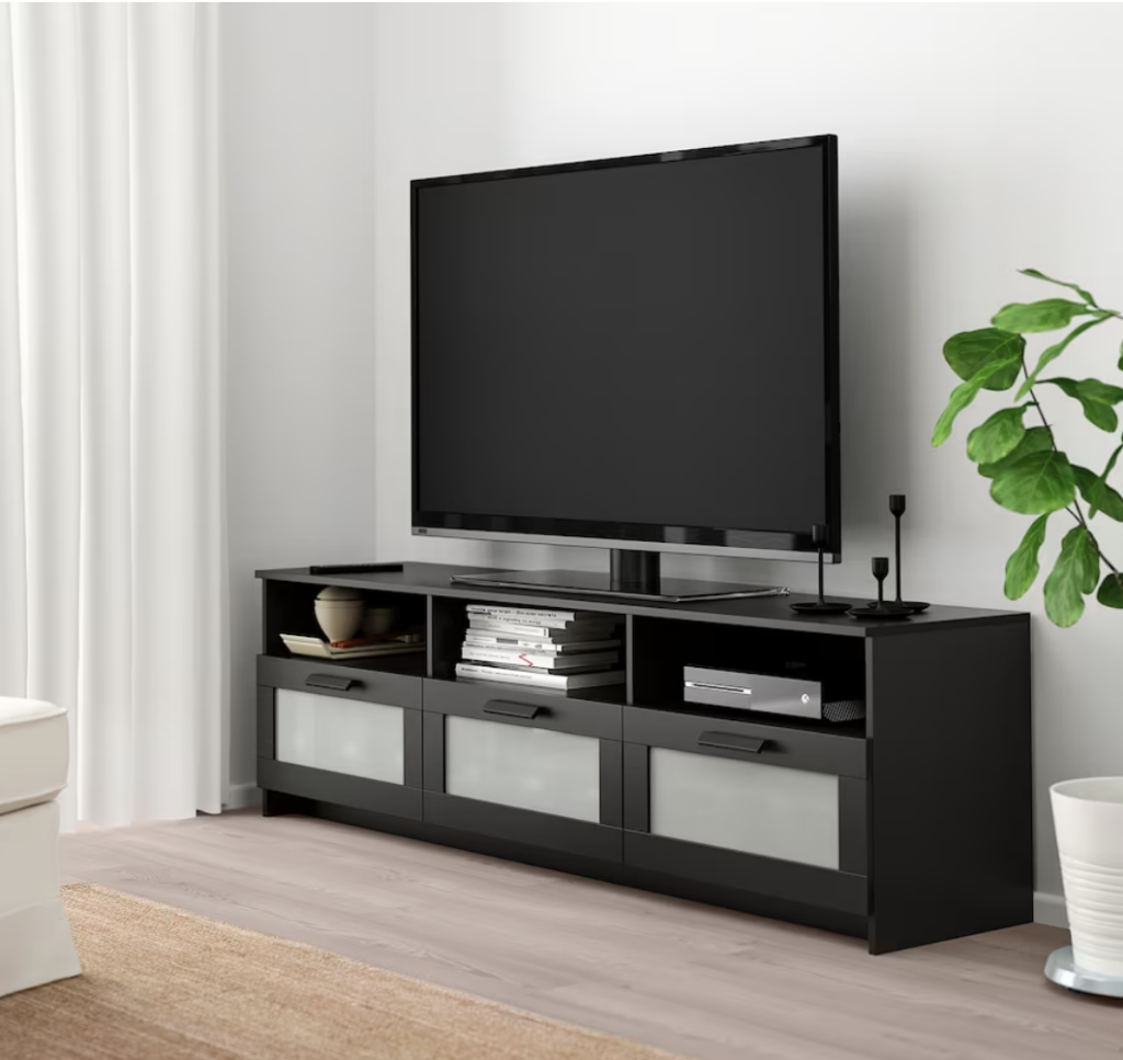 photo of a black TV stand , with a flat screen TV, and a plant on the side.