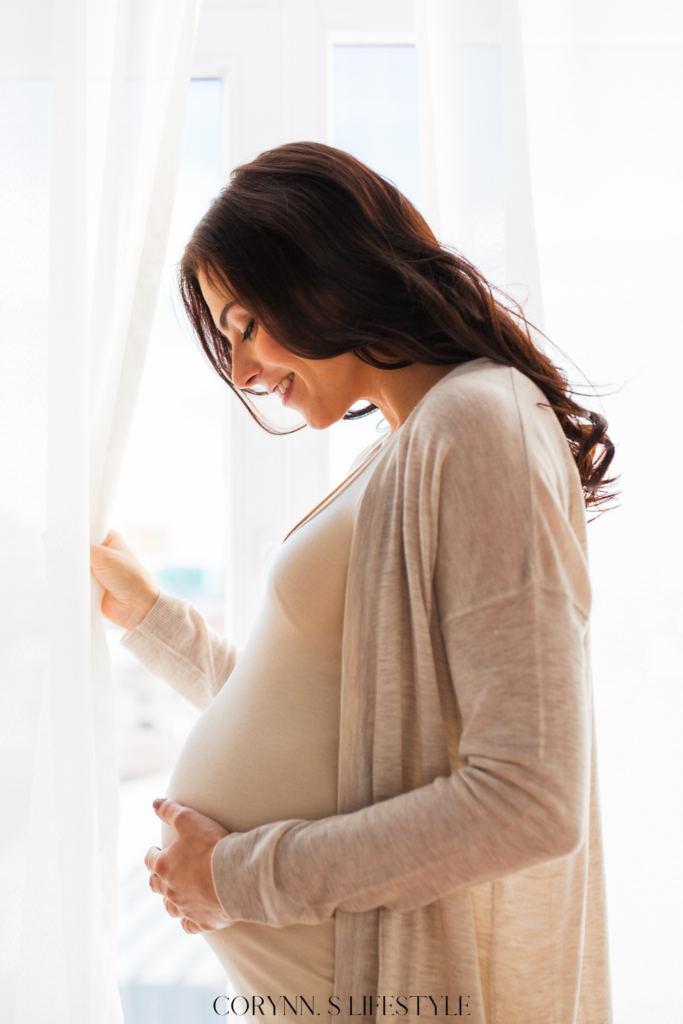 Photo of a pregnant women holding her belly near a open curtain window. Pregnant at Christmas. 