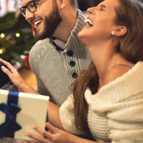photo of a couple who are holding gift while laughing. White elephant gift ideas for under $100